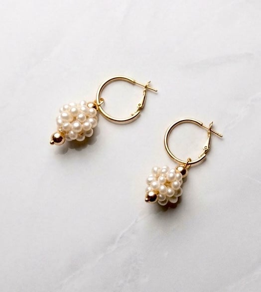 Elegant gold hoop earrings featuring a cluster pearl drop charm on a white marble background.