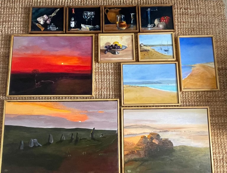 A collection of framed oil paintings featuring landscapes, coastal scenes, and still life art on a textured rug.