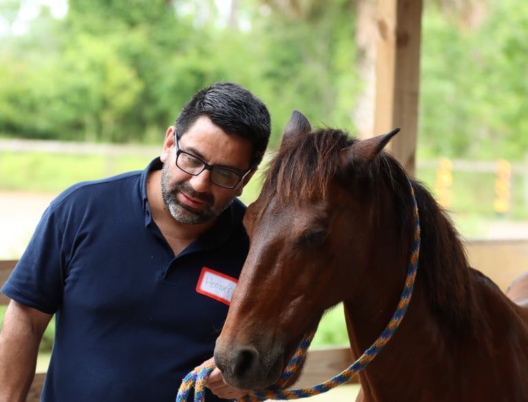 A man with glasses bonding with a brown horse during an equine therapy session.