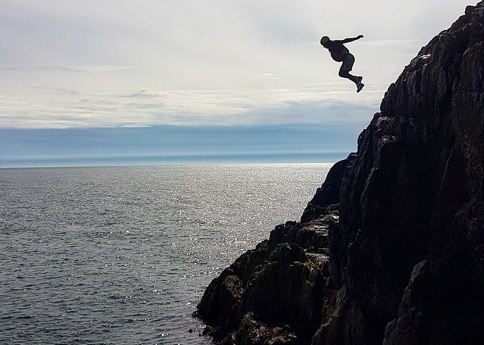 Silhouette of a person cliff jumping into the ocean on a cloudy day.
