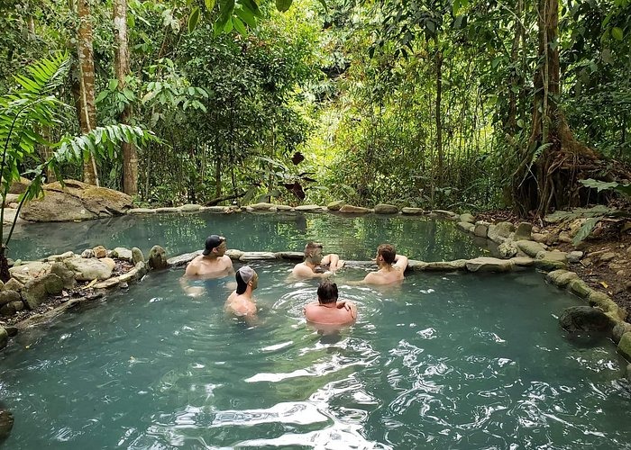 A group of men relaxing in a natural jungle hot spring pool surrounded by lush tropical rainforest.