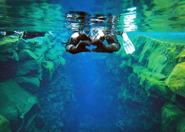A snorkeler explores the crystal clear blue water of the Silfra Fissure in Iceland between tectonic plates.