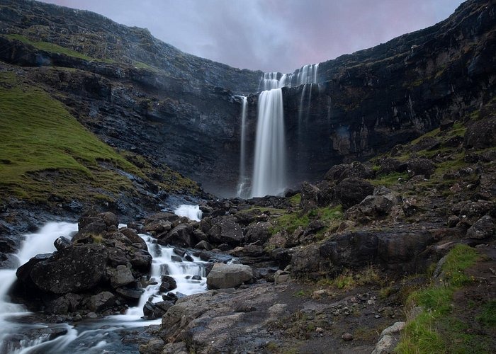 A long exposure of Fossa waterfall flowing over dark cliffs in the Faroe Islands.