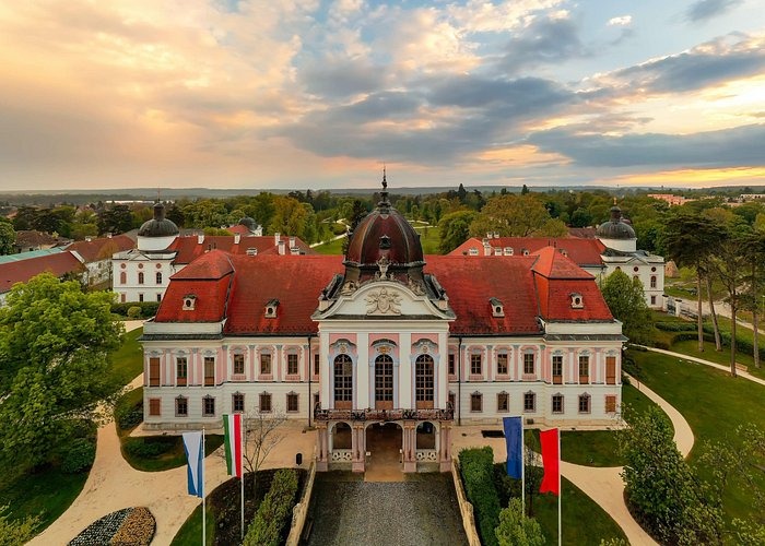Aerial view of the Royal Palace of Gödöllő in Hungary with its baroque architecture and red roof at sunset.
