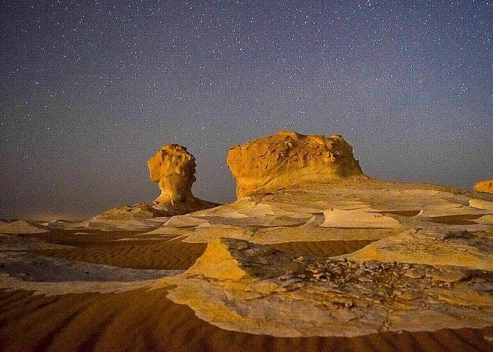 Illuminated rock formations in the White Desert National Park under a starry night sky in Egypt.