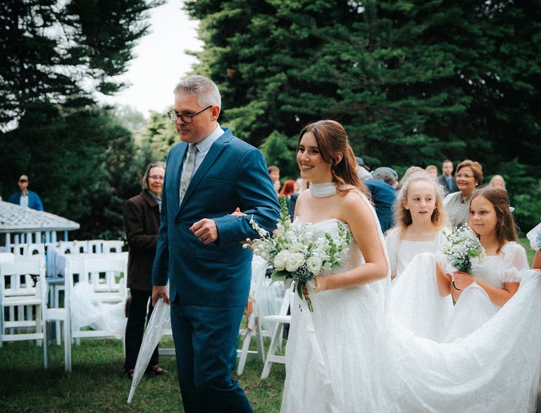 Bride arriving at the ceremony beneath the pine trees at Adelaide Botanic Garden