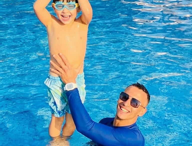 A smiling boy with goggles and a man in a blue rash guard during a fun kids swimming lesson in a pool.