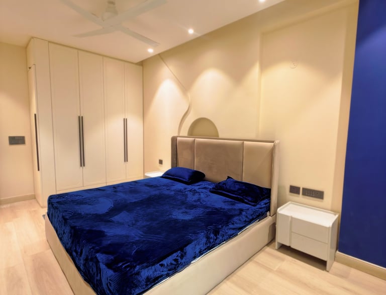 Modern master bedroom with a blue velvet bedspread, white wardrobe, and recessed lighting.