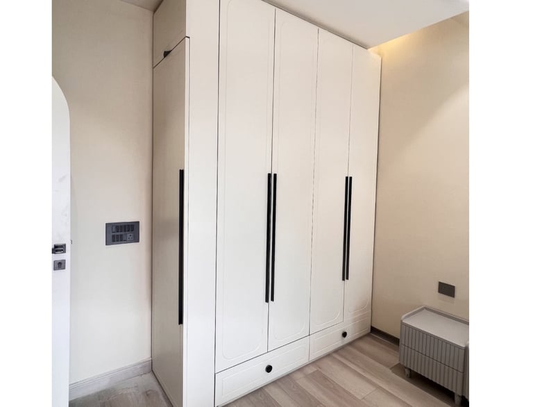 Modern white floor-to-ceiling built-in wardrobe with long black handles in a minimalist bedroom.