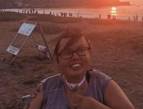 Photo of Stacey at the beach at sunset, smiling big with her hair blown by the wind. 
