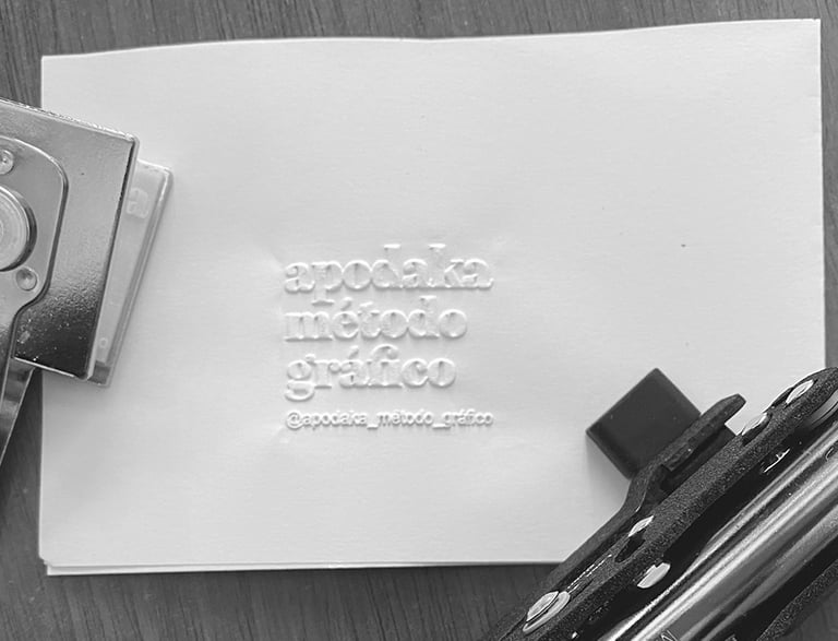 Sello metálico estampando en relieve el logotipo 'apodaka método gráfico' sobre papel blanco