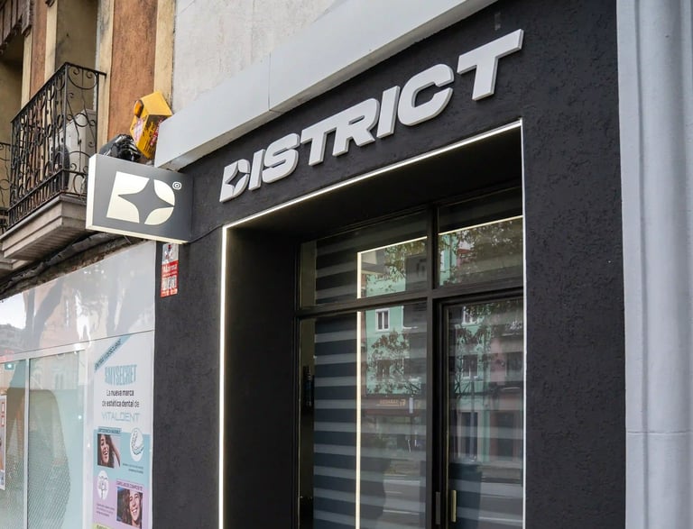 Fachada moderna y oscura de la barbería DISTRICT en Madrid, mostrando el logo y la entrada principal