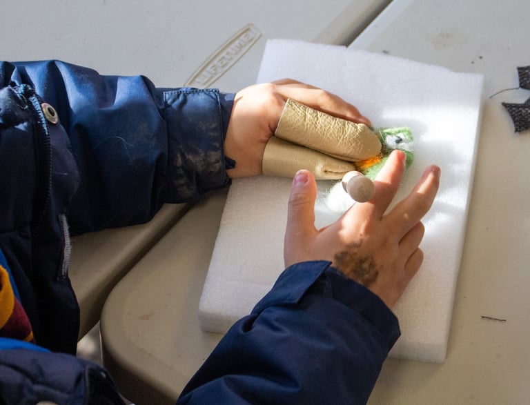 Young child's hands with finger coverings, poking pieces of wool to create a felted creature.