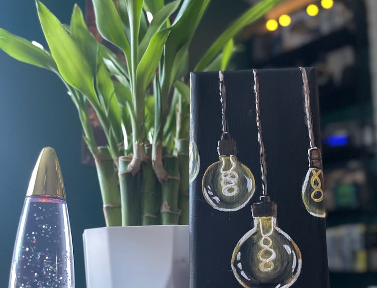 painting of lightbulbs on table with lava lamp and lucky bamboo plant