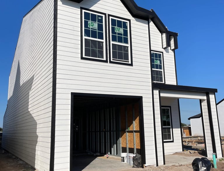 New modern two-story house construction with white lap siding and black window trim.
