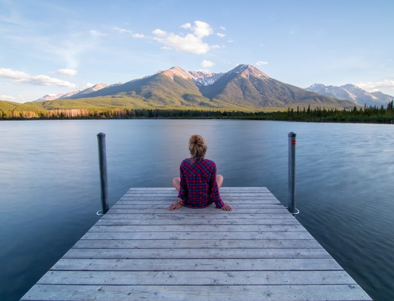 a woman sitting on a dock with mountains in the background