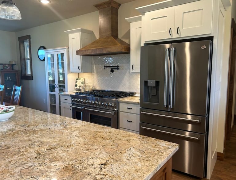 Kitchen island with granite countertop, steel refrigerator, and gas stove hood - Saddle Horn Custom