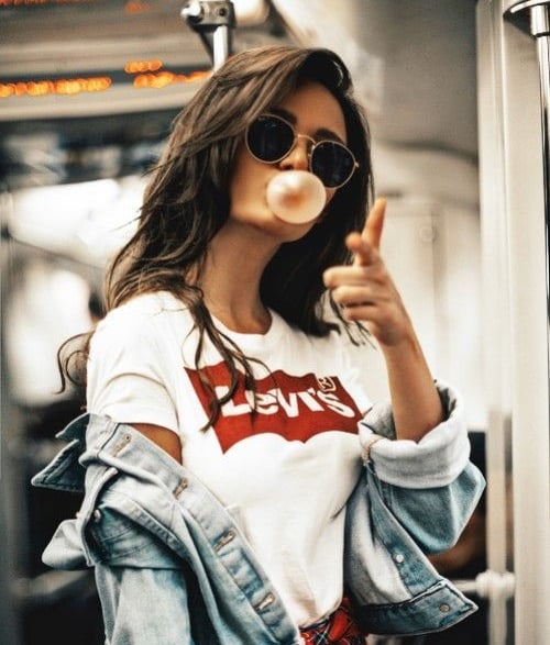 a woman in a white shirt and sunglasses blowing bubbles