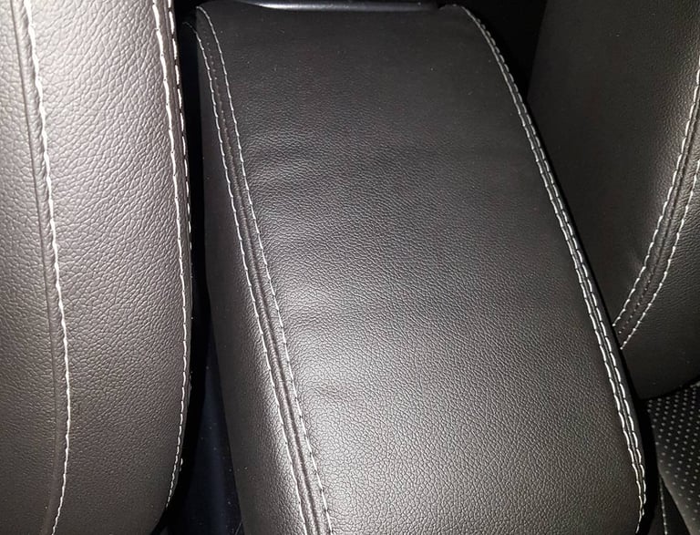 Revestimento de apoio de braço central automotivo em material escuro com costura dupla branca.