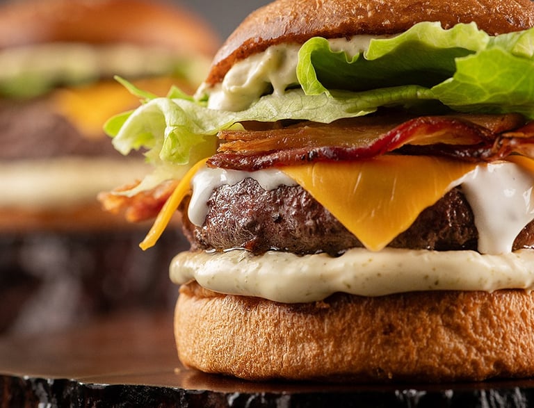 A close-up of a gourmet hamburger featuring a juicy beef patty topped with melted cheese and bacon