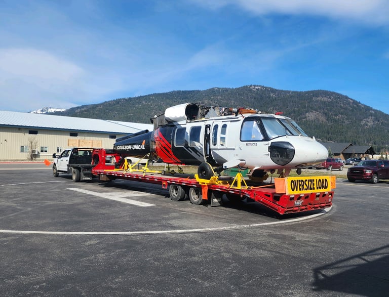 a helicopter being hauled on a long red trailer behind a truck