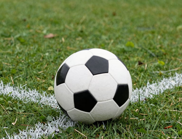 A close-up of a football on lush green grass under stadium lights at dusk.