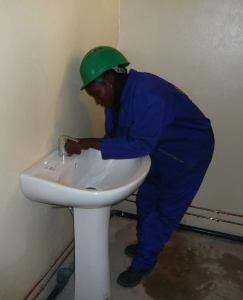Plombière en combinaison bleu installant un lavabo sur colonne dans une entreprise de Yaoundé