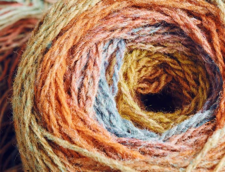 Primer plano de un ovillo de lana texturizada en tonos otoñales como naranja, dorado y azul.