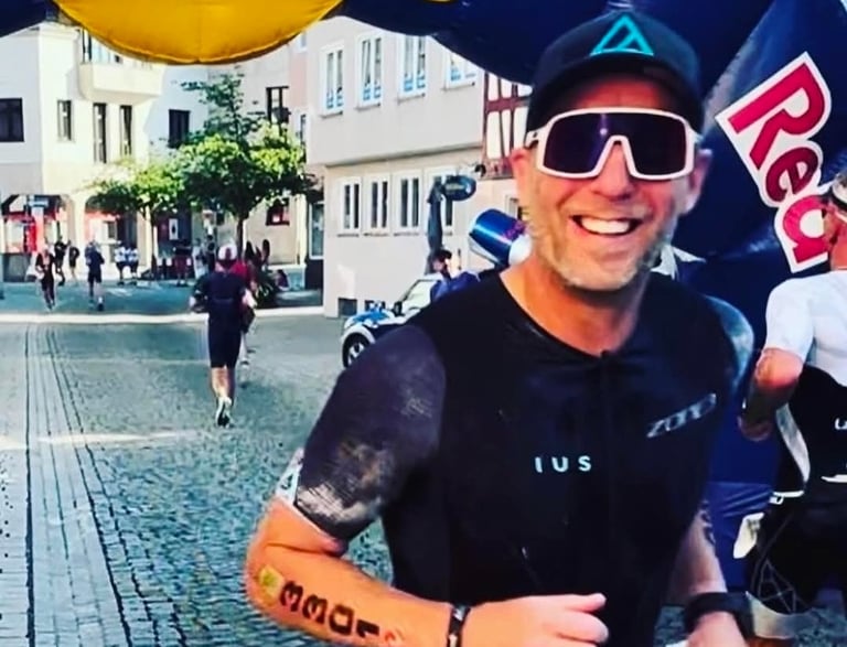 James Oswald Coaching, Doug Jones Smiling male triathlete running through a Red Bull arch during.