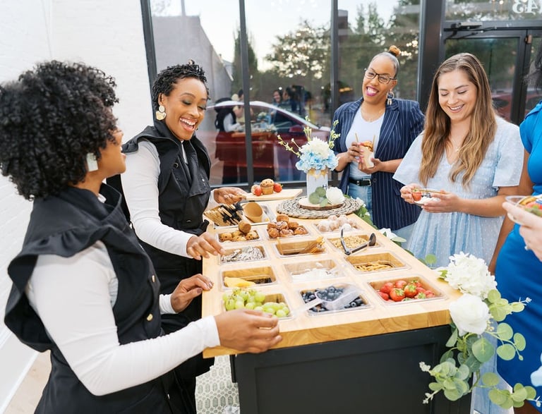 a group of people standing around a table with food