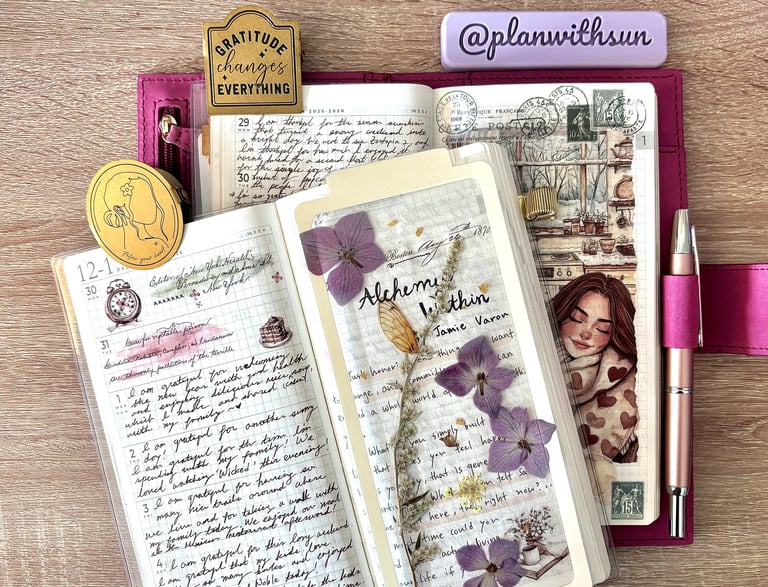 Open journaling notebook with handwritten entries, dried purple flowers, and stationery on a desk.
