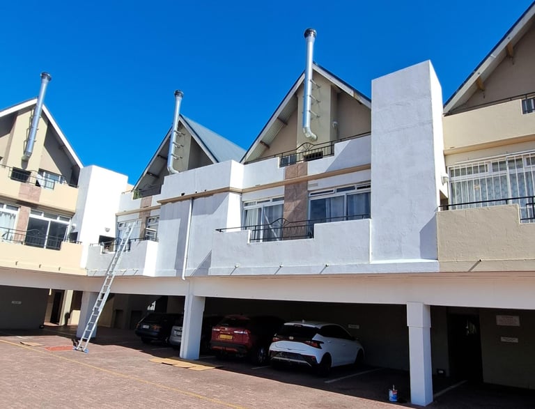 Modern multi-story apartment complex with covered parking and silver chimney flues under a clear blue sky.