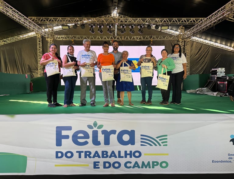 pessoas alinhadas em um palco com cada uma segurando uma sacola estampada com “Feira do trabalho"