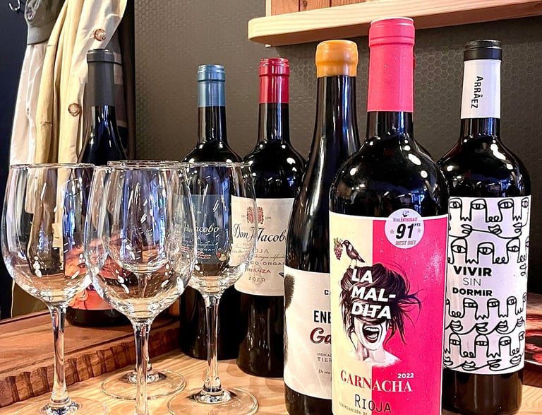 Four wine glasses lined up in front of four bottles of red Spanish wine