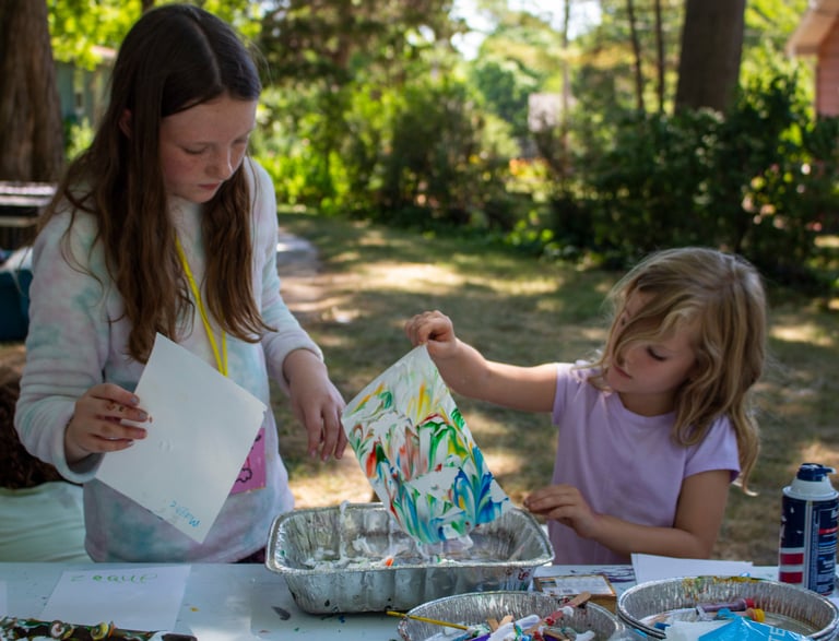 Two young girls lifting pieces of paper from a container to reveal colorful, marbled pieces.