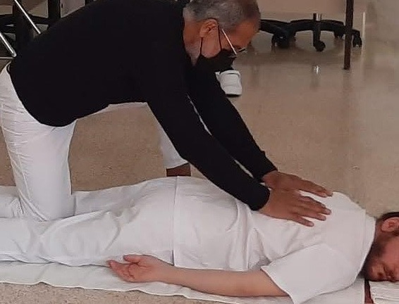 Un hombre está realizando un masaje de espalda a una clienta que está tumbada en el suelo sobre una 