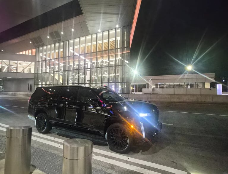 Black luxury Cadillac Escalade SUV parked at night outside a modern glass airport terminal.