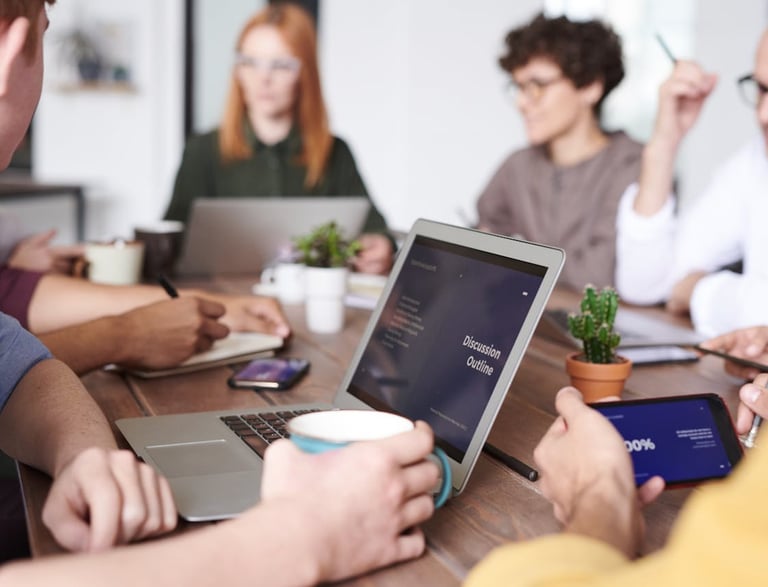 a group of people sitting around a table with laptops