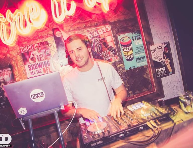 DOXIS djing in front of a neon sign