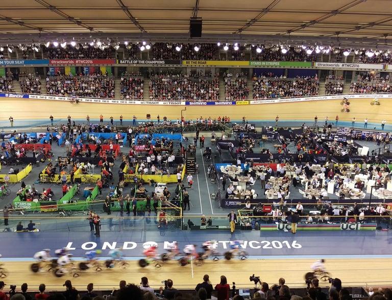 a group of people riding bicycles in a velodrome with lots of spactators