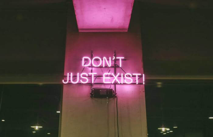Neon sign reading “Don’t just exist” glowing in a dark room.