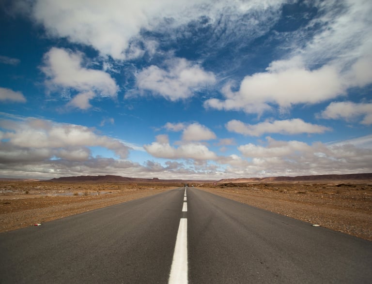 A Moroccan desert road with painted white lines receding into the distance