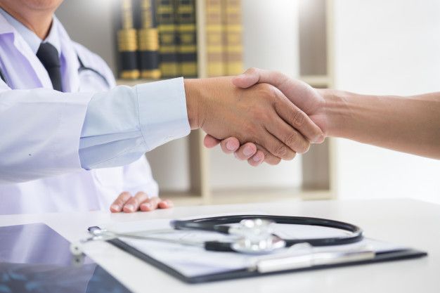 Profissional da saúde em consultório apertando a mão do paciente