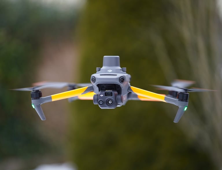 Professional DJI Mavic 3 Enterprise drone with RTK module hovering outdoors against a blurred forest background.