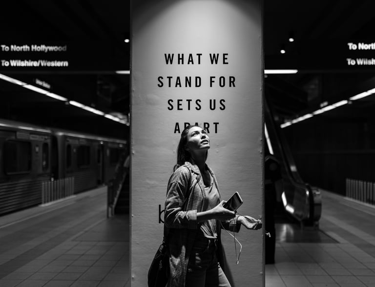 grayscale photo a woman standing in a subway station next to a social impact ad