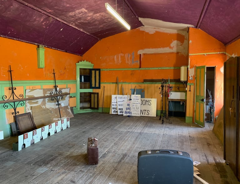 Old school hall with orange walls, storage units, and exposed structure pre-conversion.