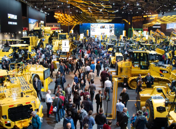 a large group of people standing around a large group of yellow construction equipment