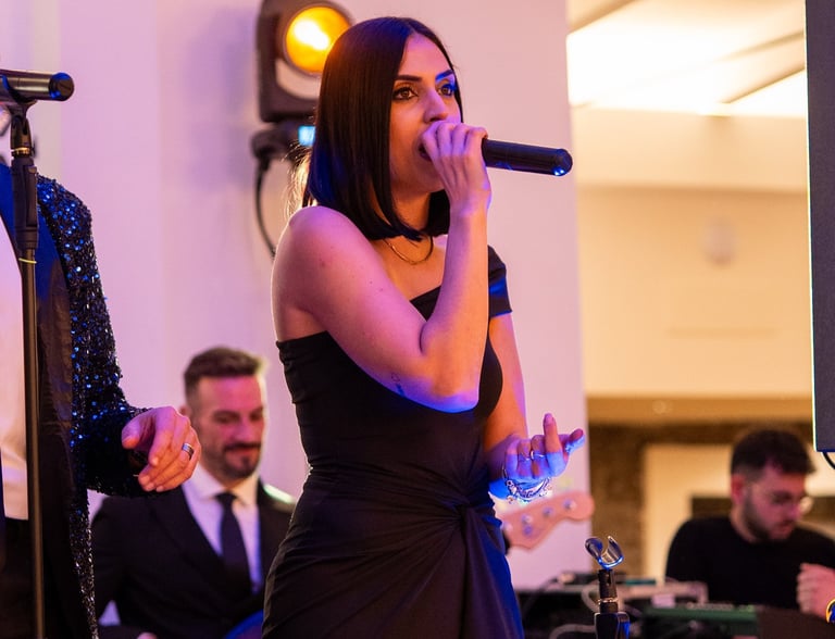 Female lead singer in a black dress performing with a live wedding band at a gala event.
