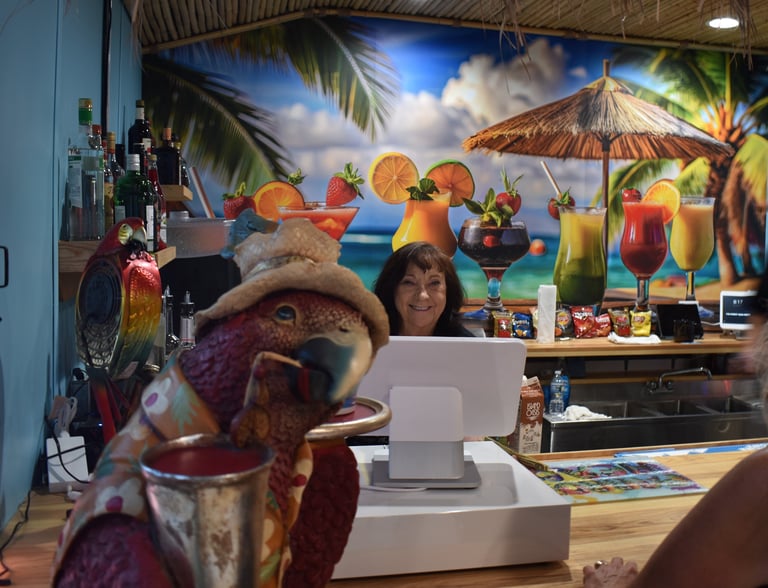 Image of female owner working behind cash register with image of tropical drink behind her.