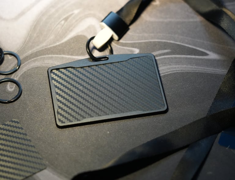 Black carbon fiber ID badge holder with a neck lanyard and key rings on a desk.